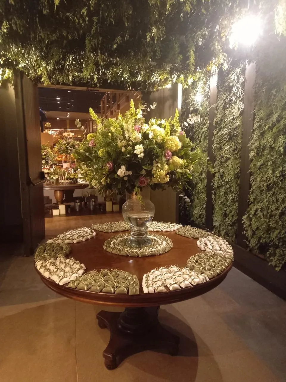 Bem casados em papel verde-oliva e creme, dispostos em mesa redonda decorada com arranjo floral