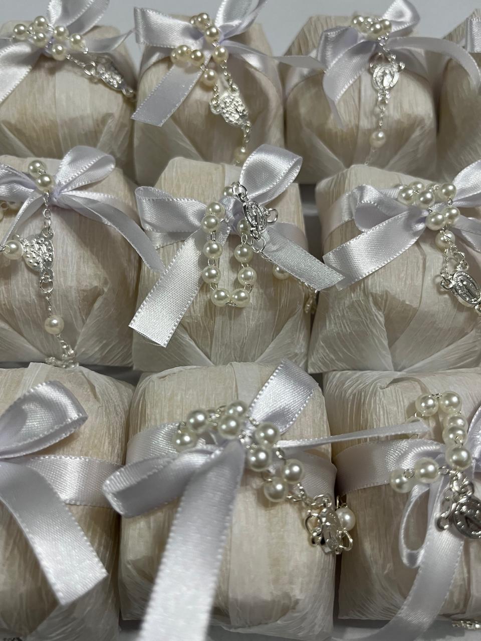 Bem casados embalados em papel off-white com laço branco e mini terço de pérolas