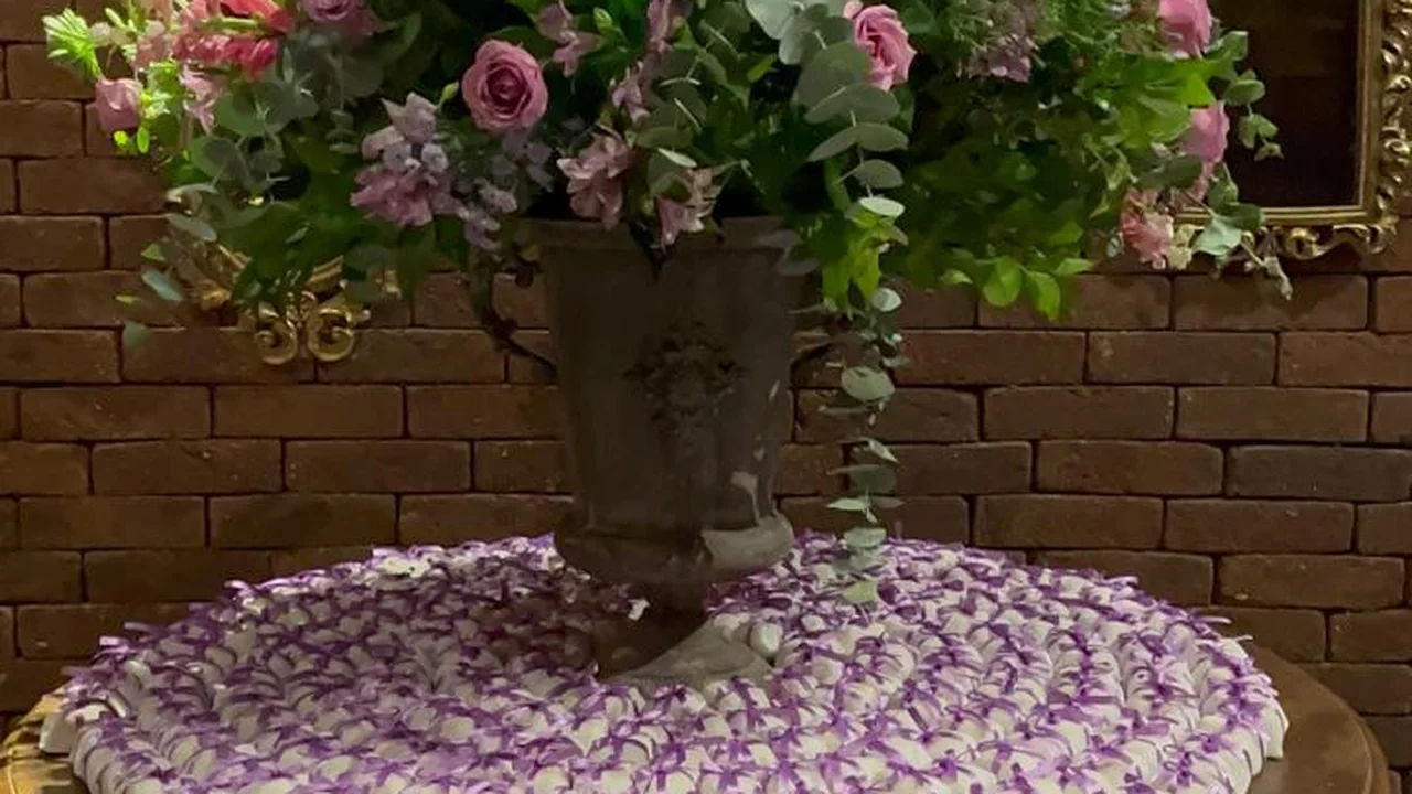 Centenas de bem casados embalados em branco com laço lilás, em mesa decorada com arranjo floral