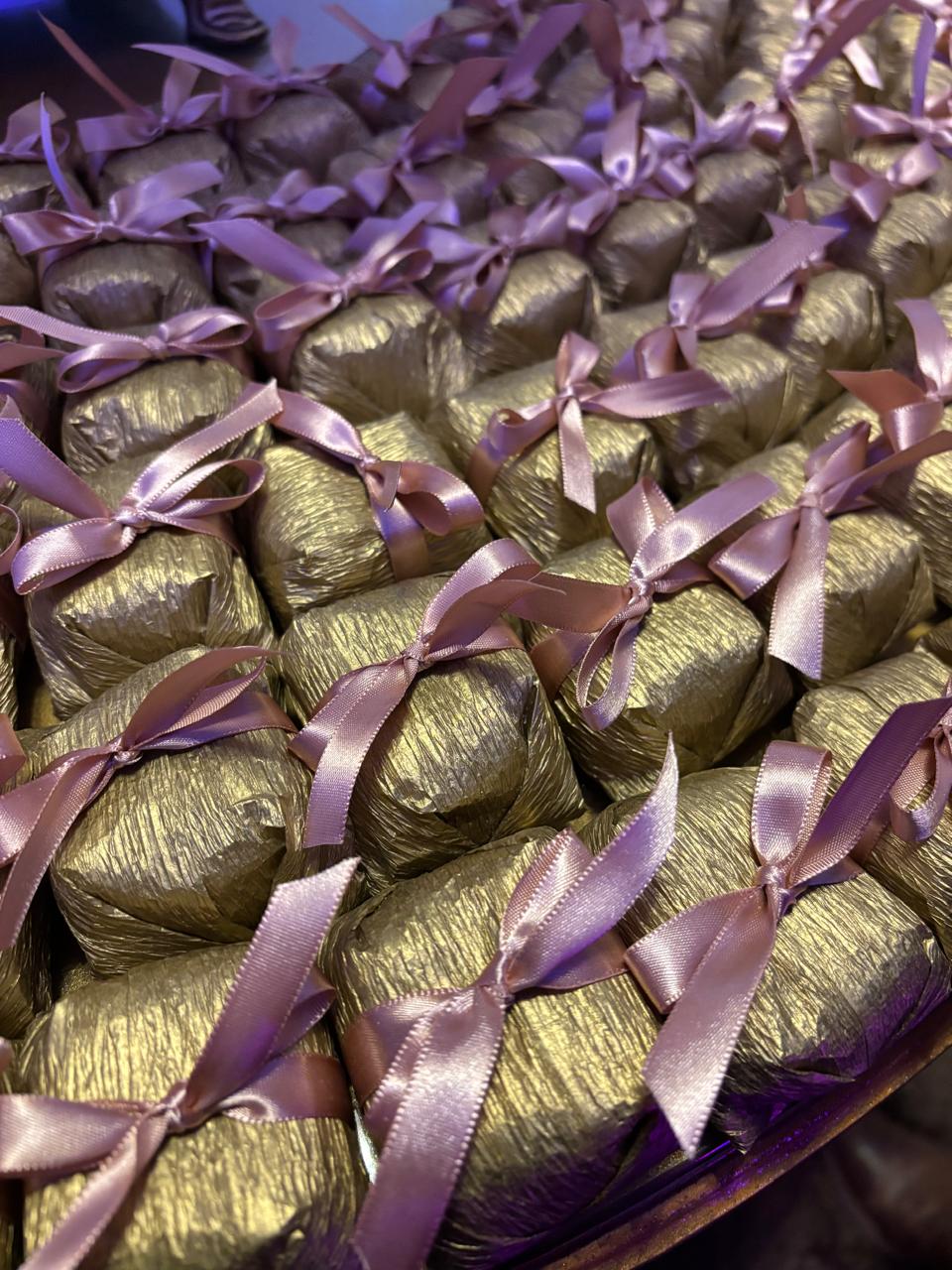 Bem casados embalados em papel dourado com laço de fita de cetim rosê