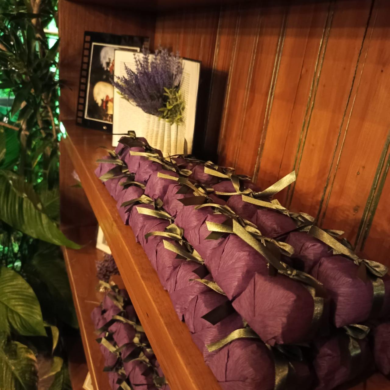 Bem casados embalados em roxo com laço verde-oliva, empilhados em prateleira de madeira