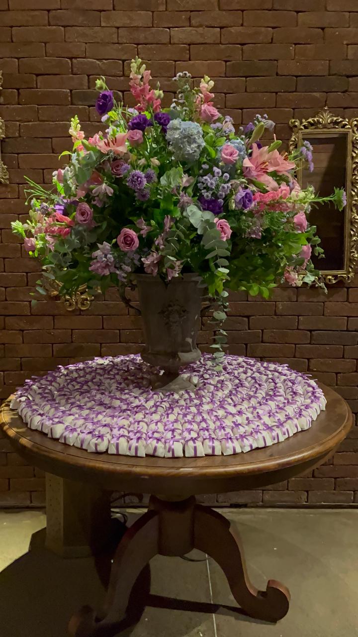 Centenas de bem casados embalados em branco com laço lilás, em mesa decorada com arranjo floral