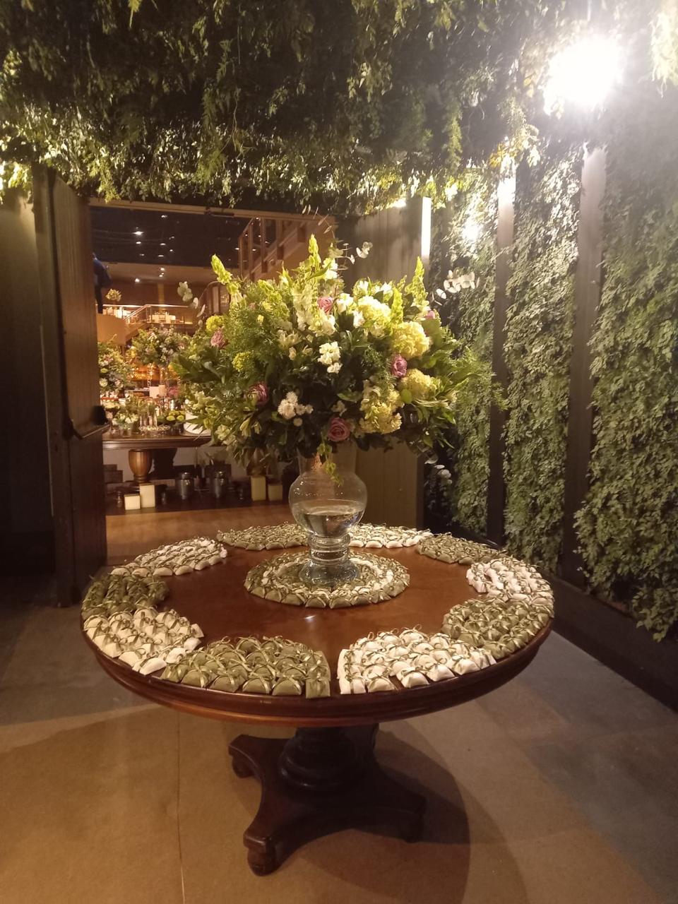 Bem casados em papel verde-oliva e creme, dispostos em mesa redonda decorada com arranjo floral