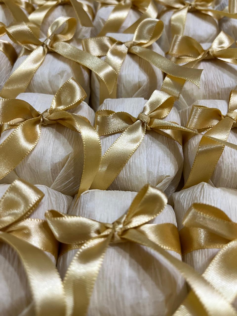Bem casados embalados em papel branco marfim, com fita e laço de cetim dourado