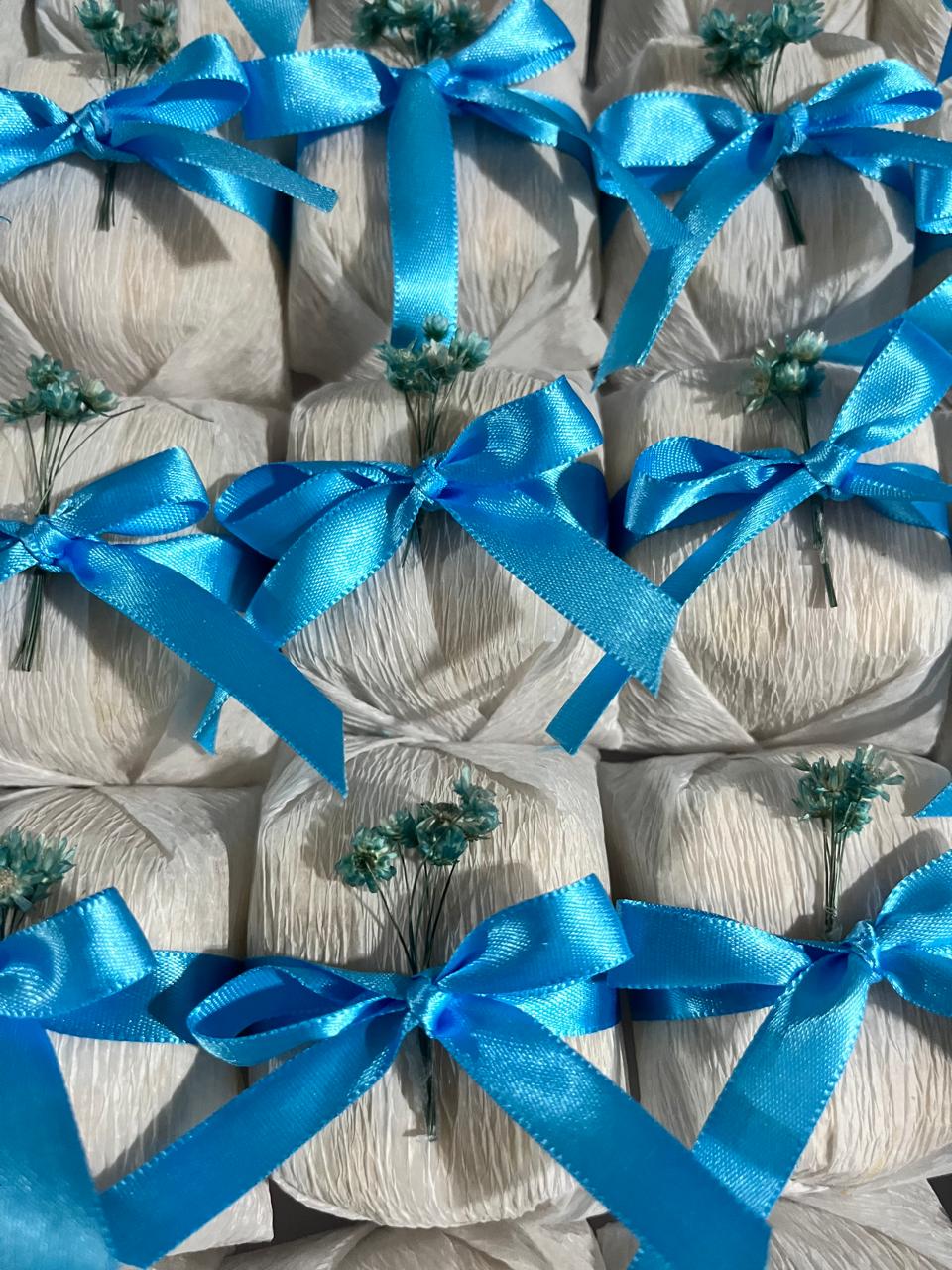 Bem casados embalados em papel branco com laço azul e raminhos de flores secas azuis